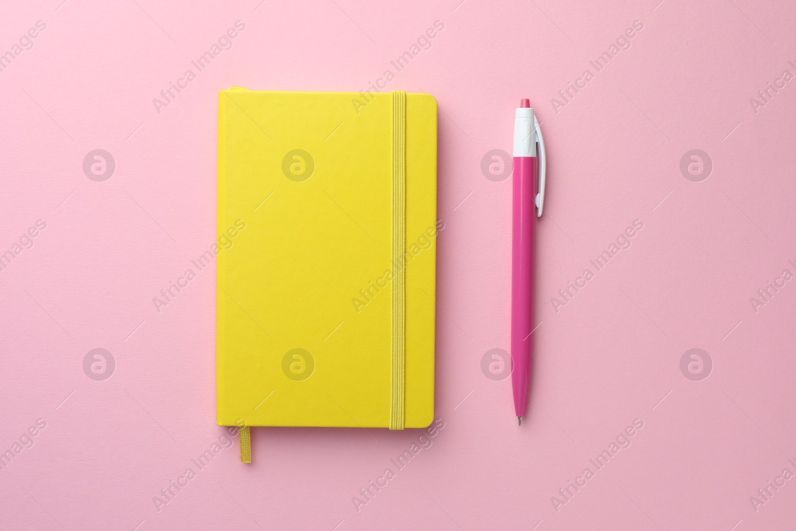 Photo of Closed yellow notebook and pen on light pink background, top view