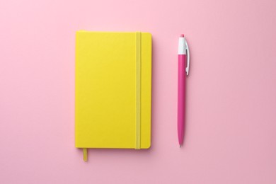 Photo of Closed yellow notebook and pen on light pink background, top view