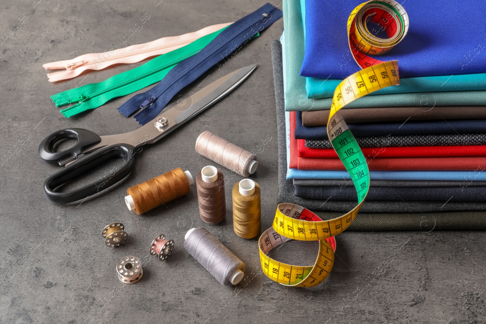 Photo of Bobbins with threads, measuring tape and stack of colorful fabrics on table. Tailoring accessories