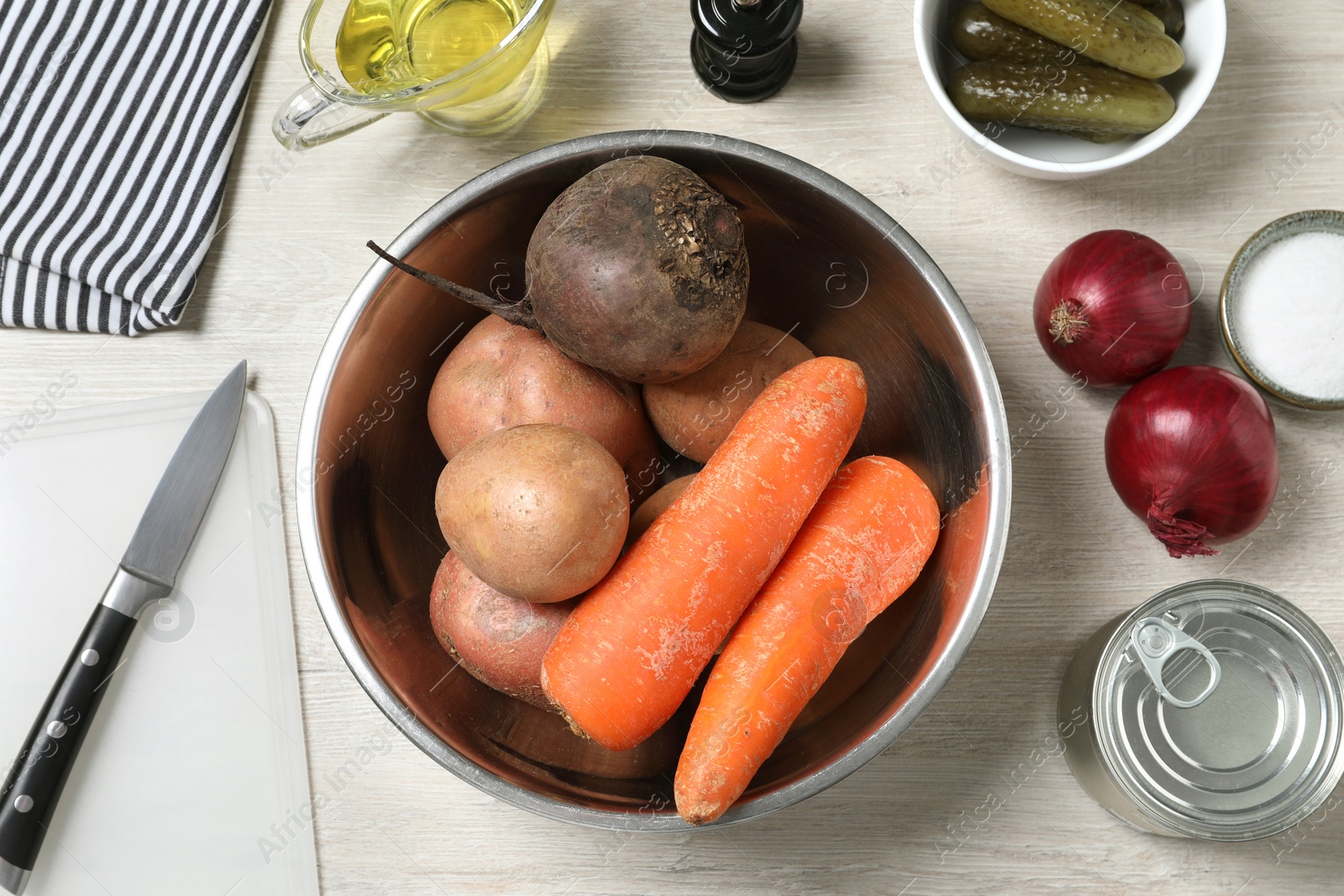 Photo of Bowl with many fresh vegetables and other ingredients on white wooden table, flat lay. Cooking vinaigrette salad