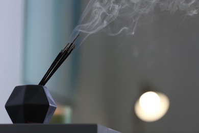 Photo of Incense sticks smoldering on table indoors, space for text