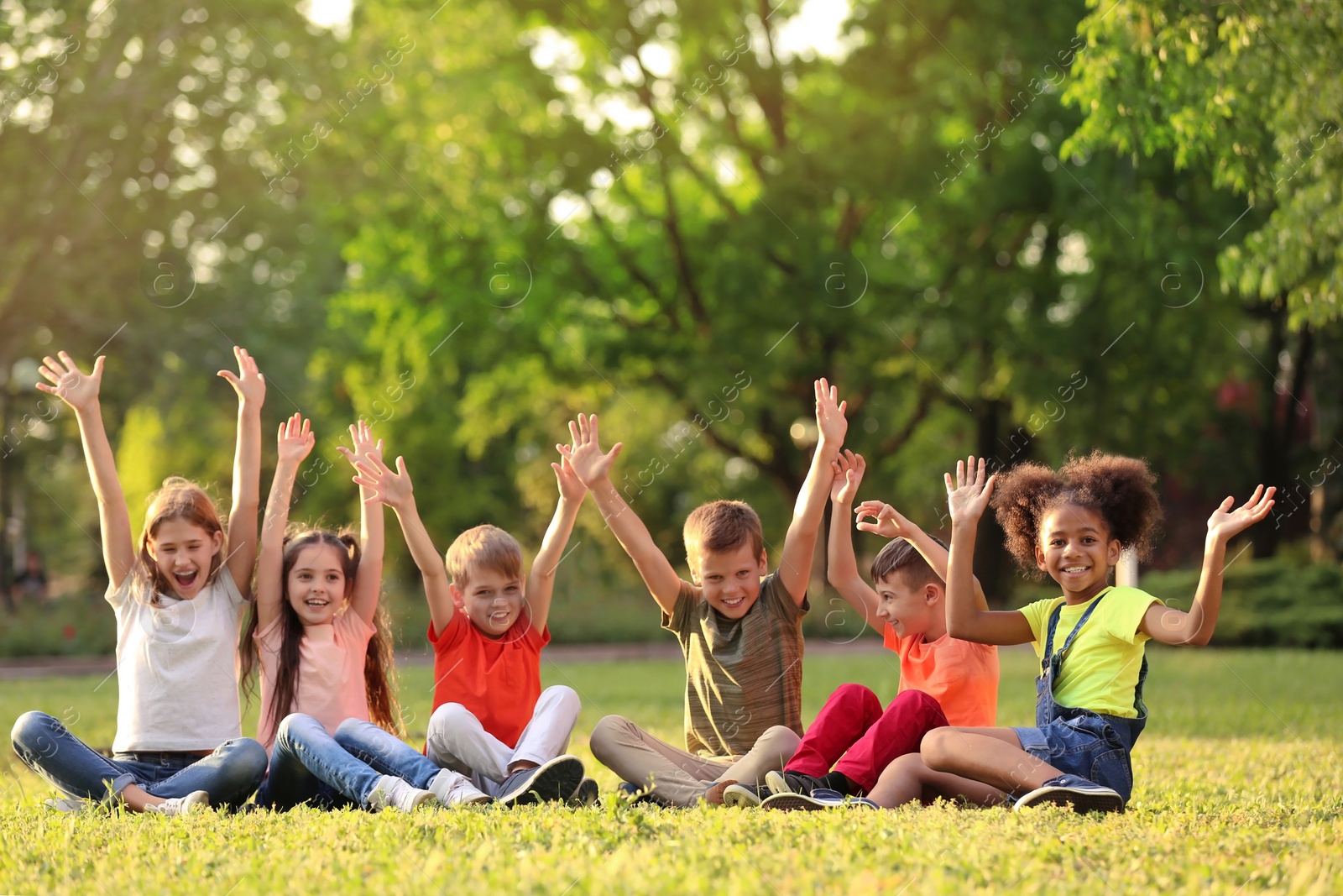 Photo of Cute little children sitting on grass outdoors on sunny day