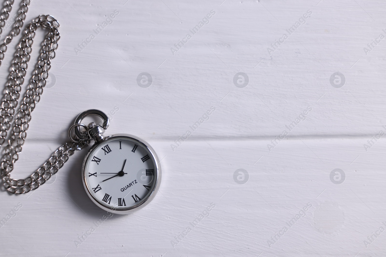 Photo of Silver pocket clock with chain on white wooden table, top view. Space for text