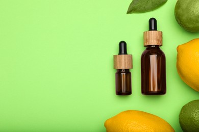 Photo of Bottles of citrus essential oil and fresh fruits on green background, flat lay. Space for text