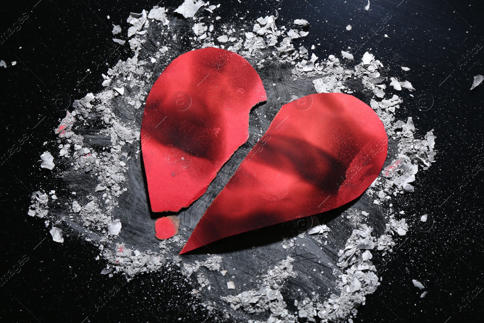 Photo of Halves of torn paper heart and ash on black background, above view