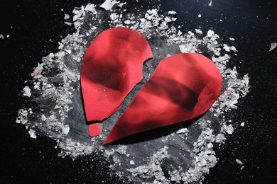 Photo of Halves of torn paper heart and ash on black background, above view