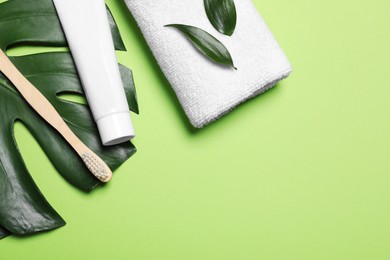 Photo of Toothpaste, brush, leaves and towel on light green background, flat lay. Space for text