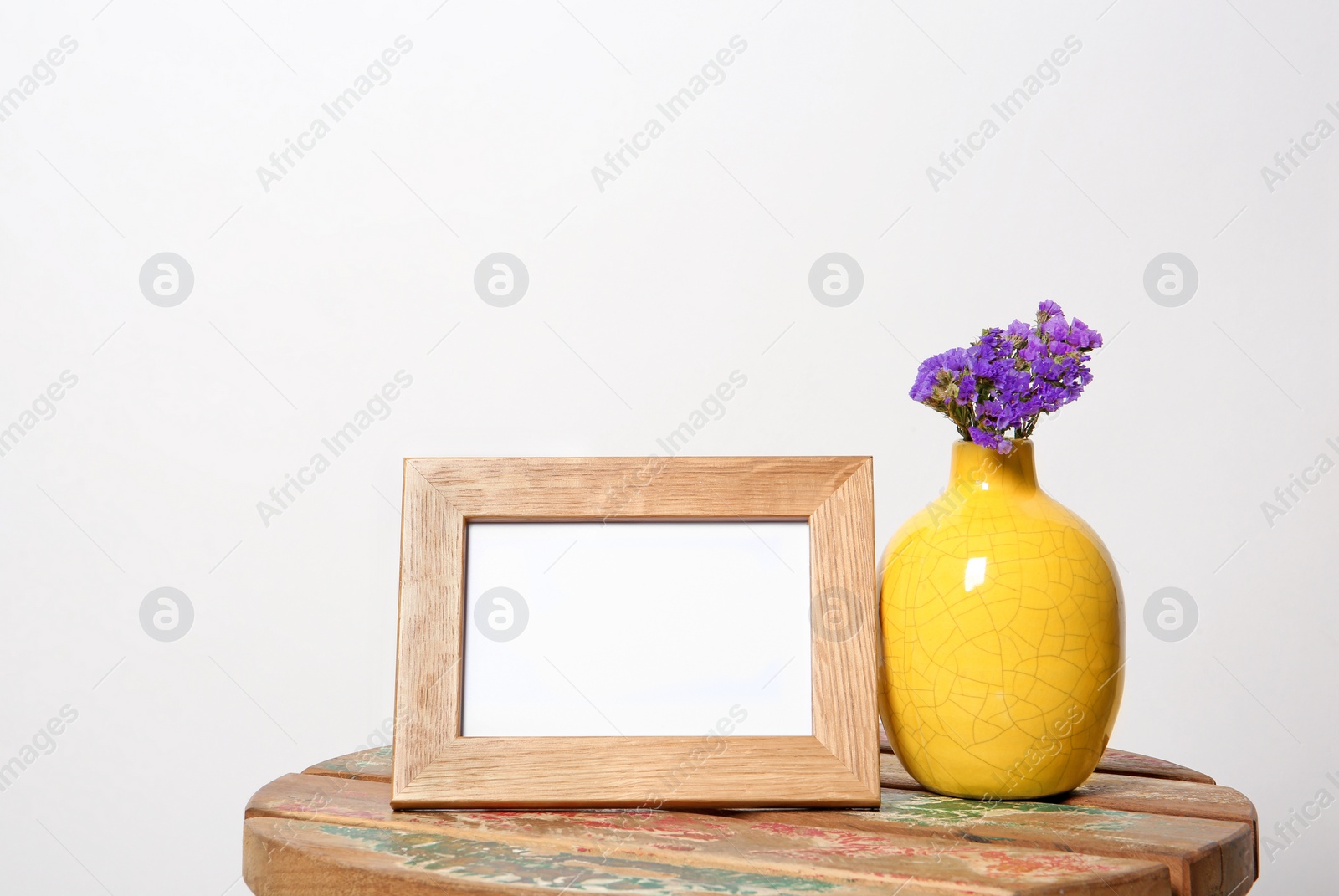 Photo of Blank frame and vase with flowers on table against white background. Mock up for design