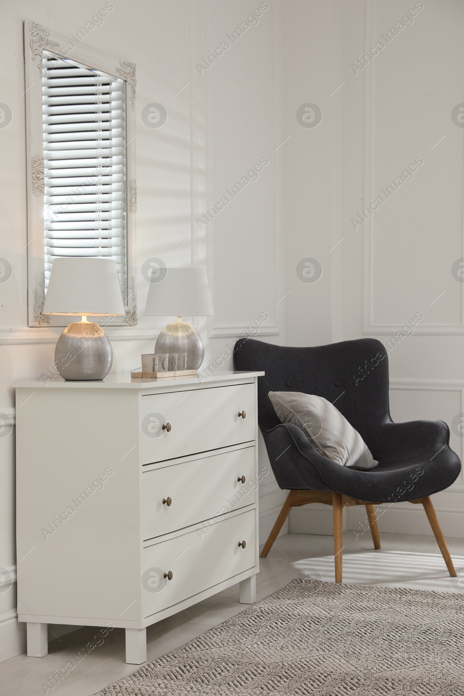 Photo of White chest of drawers, armchair and mirror in room. Interior design