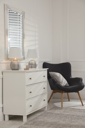 White chest of drawers, armchair and mirror in room. Interior design