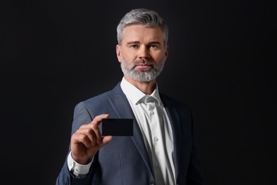 Handsome businessman holding blank business card on black background