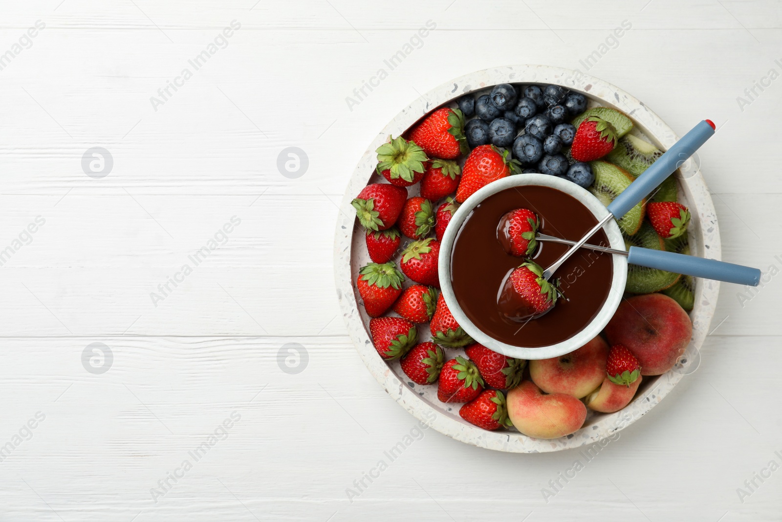 Photo of Fondue pot with chocolate and mix of fruits on white wooden table, top view. Space for text