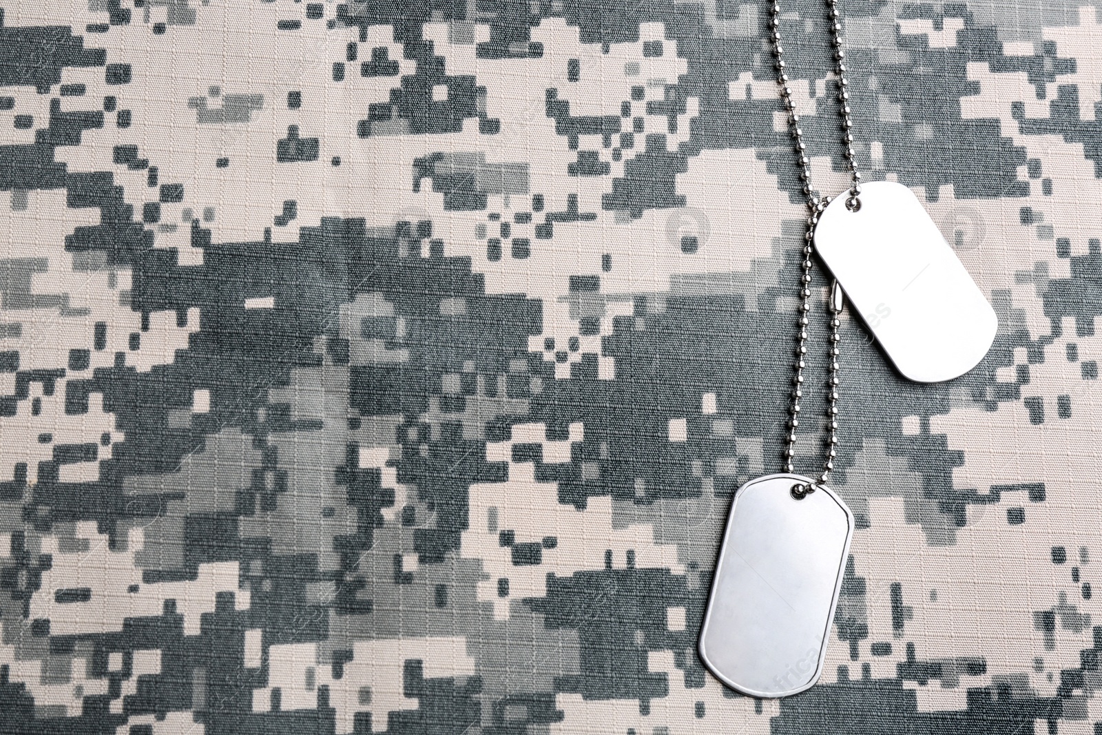 Photo of Military ID tags on camouflage background, top view. Space for text