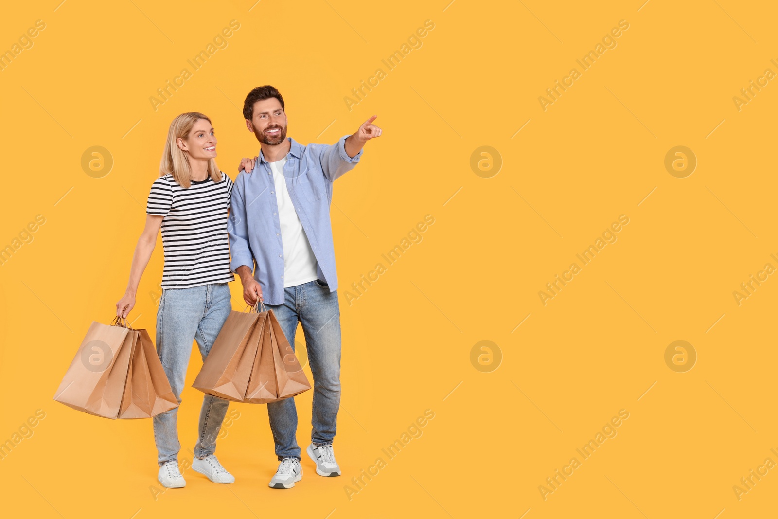 Photo of Family shopping. Happy couple with paper bags on orange background. Space for text