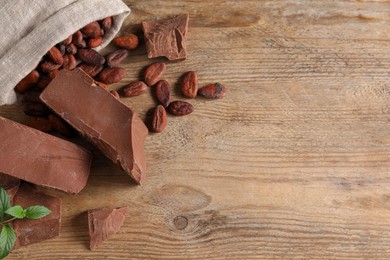 Pieces of tasty milk chocolate, cocoa beans and mint on wooden table, flat lay. Space for text