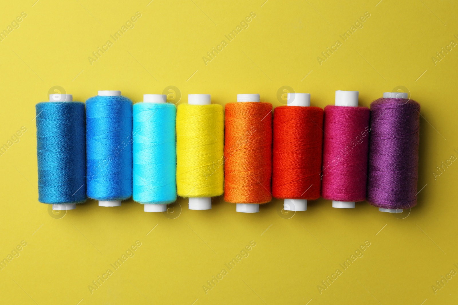 Photo of Set of different colorful sewing threads on yellow background, flat lay