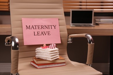 Photo of Baby care accessories, notebooks and note with text Maternity Leave on office chair indoors