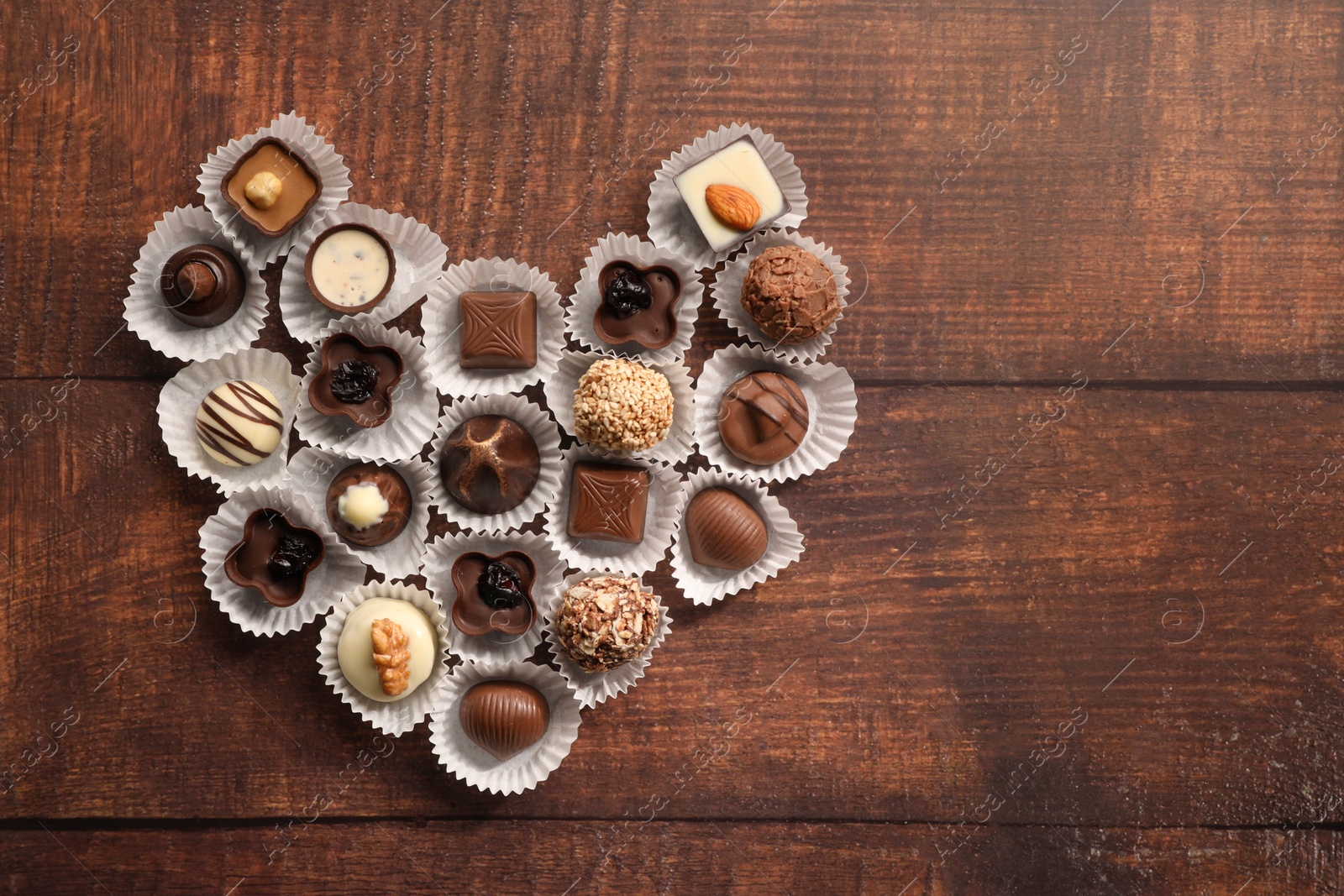 Photo of Heart made with delicious chocolate candies on wooden table, top view. Space for text