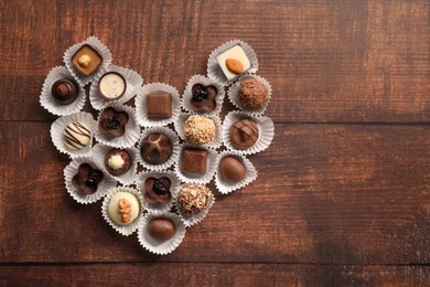 Heart made with delicious chocolate candies on wooden table, top view. Space for text