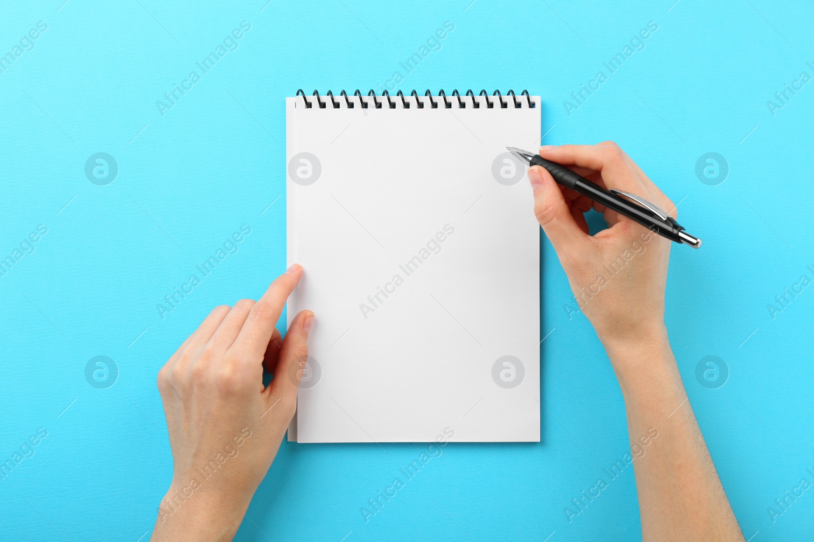 Photo of Woman writing in notebook on light blue background, top view