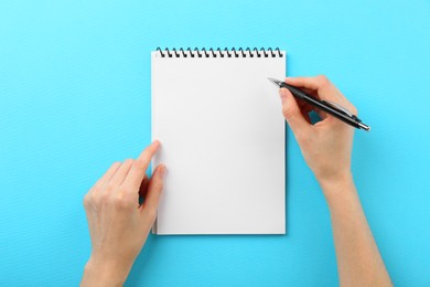 Photo of Woman writing in notebook on light blue background, top view