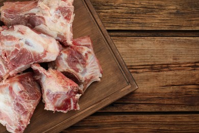 Photo of Cutting board with raw chopped meaty bones on wooden table, top view. Space for text