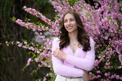 Beautiful young woman near blossoming sakura tree on spring day, space for text