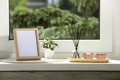 Photo of Blank photo frame with reed diffuser and home decor on white window sill