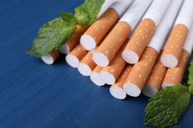 Photo of Menthol cigarettes and mint leaves on blue wooden table, closeup. Space for text