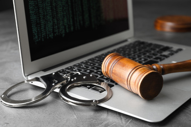 Laptop, wooden gavel and handcuffs on grey table, closeup. Cyber crime
