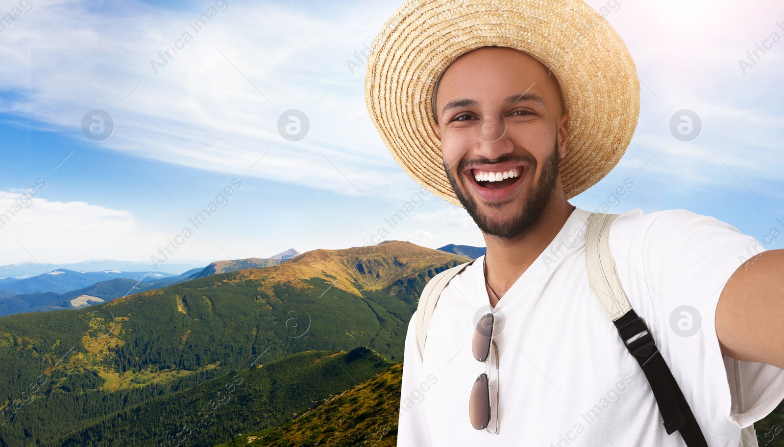 Image of Smiling young man in straw hat taking selfie in mountains