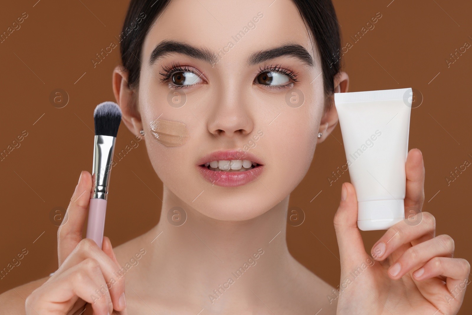 Photo of Teenage girl with tube of foundation and brush on brown background