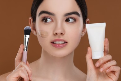 Teenage girl with tube of foundation and brush on brown background