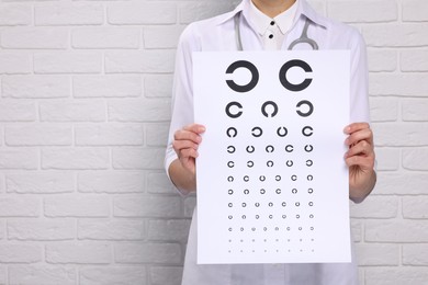 Photo of Ophthalmologist with vision test chart near white brick wall, closeup Space for text