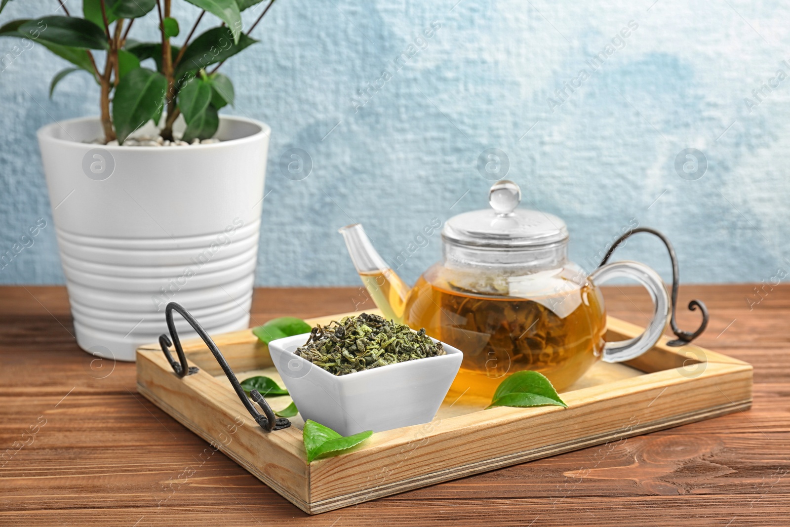 Photo of Wooden tray with hot aromatic tea, dry and fresh leaves on wooden table