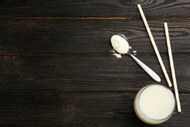 Protein shake, powder and straws on black wooden table, flat lay. Space for text