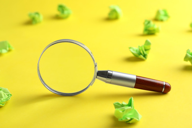 Magnifier glass and green crumpled paper sheets on yellow background, closeup. Find keywords concept