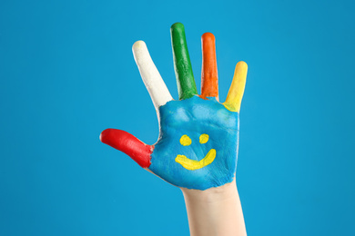 Photo of Kid with smiling face drawn on palm against blue background, closeup