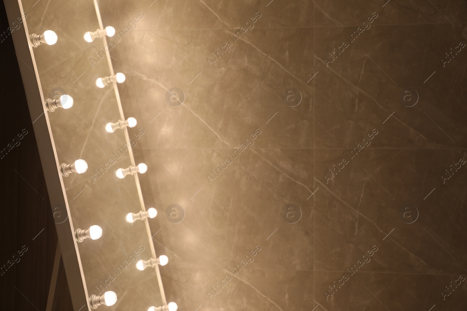 Photo of Modern mirror with light bulbs near brown wall, closeup. Space for text