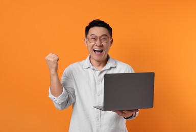 Emotional man with laptop on orange background