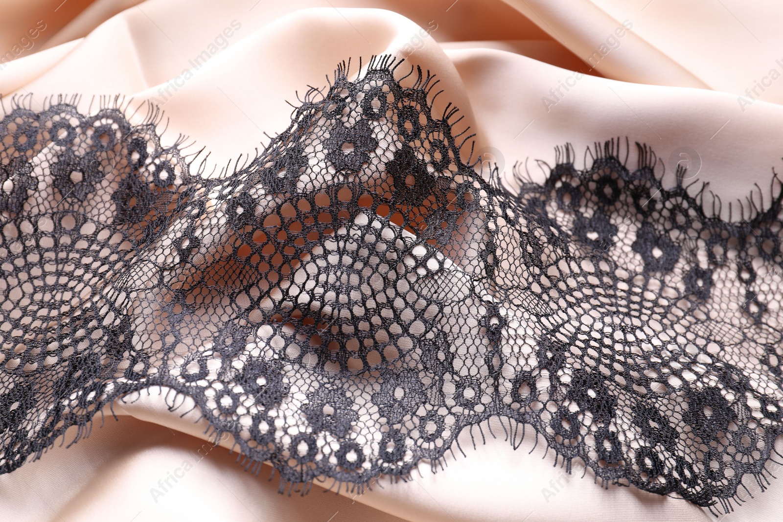 Photo of Beautiful black lace on beige fabric, top view