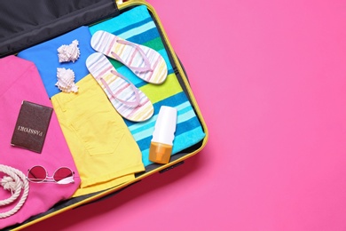 Photo of Open suitcase with beach objects on pink background, top view. Space for text