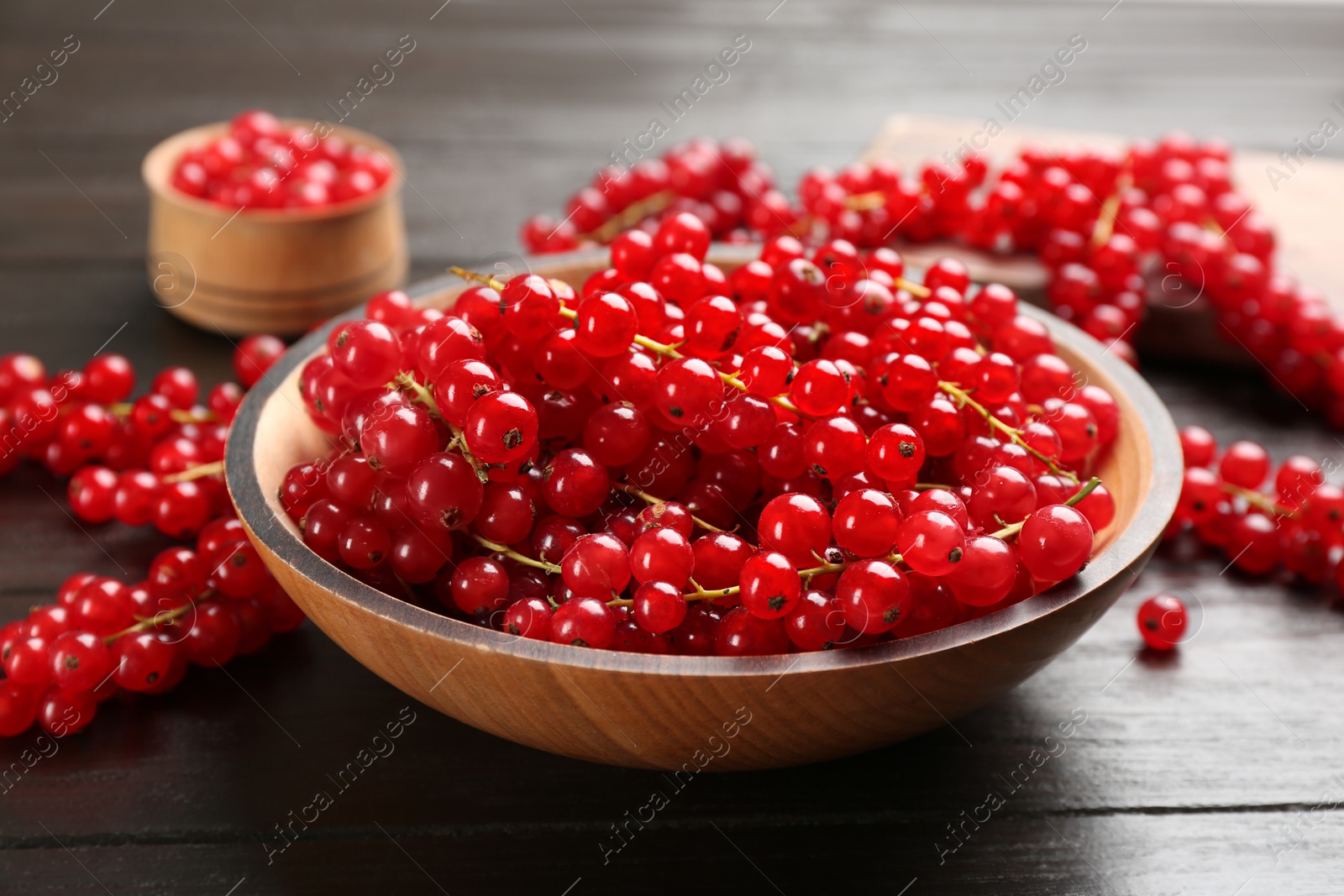 Photo of Delicious red currants in bowl on dark wooden table