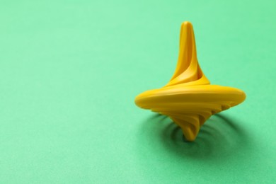 Photo of One yellow spinning top on green background, closeup. Space for text