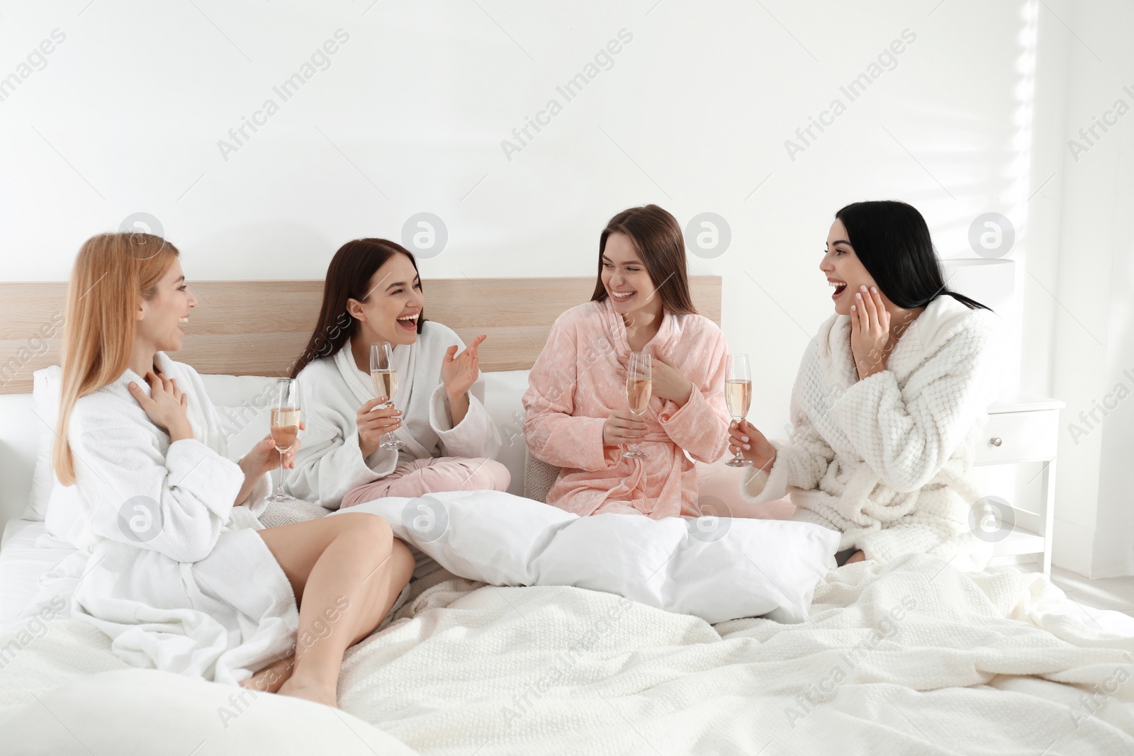 Photo of Beautiful young ladies with champagne on bed at pamper party. Women's Day