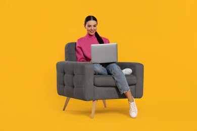 Photo of Happy woman with laptop sitting in armchair on orange background