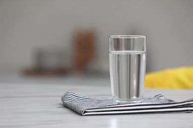 Photo of Glass of water and napkin on white table against blurred background. Space for text