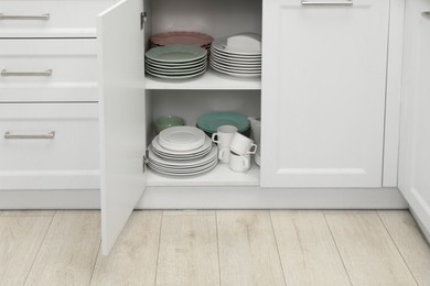 Clean plates and other crockery on shelves in cabinet indoors