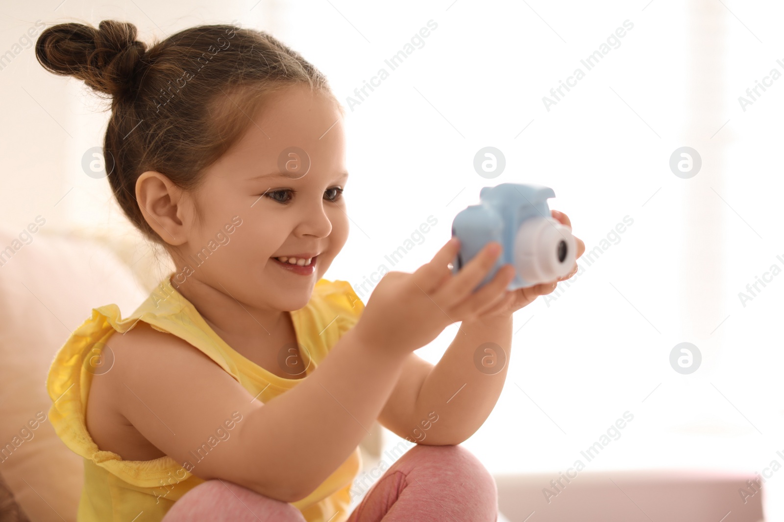 Photo of Little photographer taking picture with toy camera on sofa at home