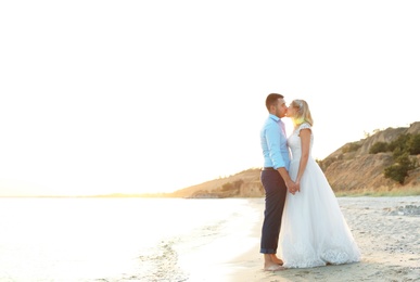 Photo of Wedding couple holding hands and kissing on beach. Space for text